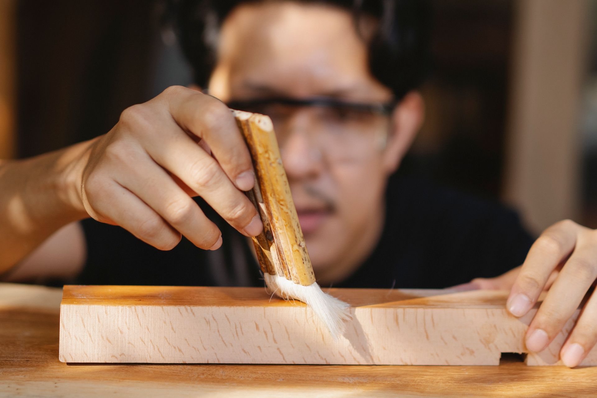 A craftsman brushing oil onto a length of pale wood.